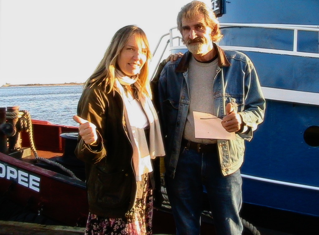 Woman and man standing on the foredeck of a tug boat.